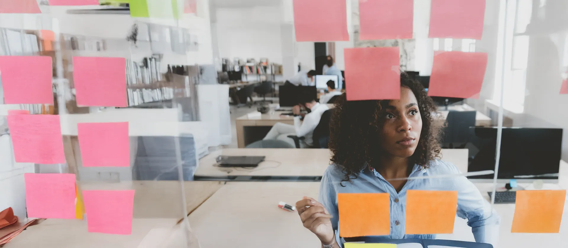 Afroamerikanische Mitarbeiterin, die auf eine Glaswand mit Haftnotizen blickt, Rahmenwerk für das Arbeitsmanagement, Scrum-Methodik 