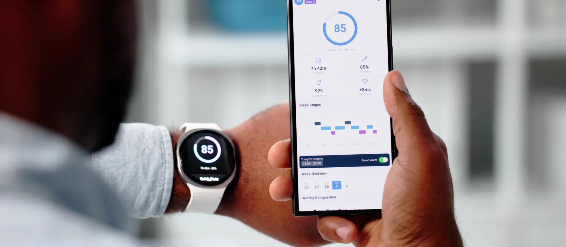 Person betrachtet Schlaf- und Gesundheitsdaten auf einem Smartphone, das mit einer Smartwatch verbunden ist.