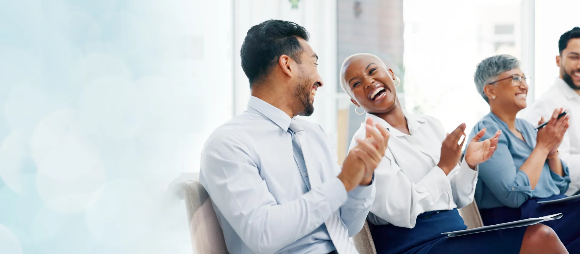 Group of people applauding and laughing in a bright room, symbolizing successful projects, teamwork and positive outcomes for success stories.