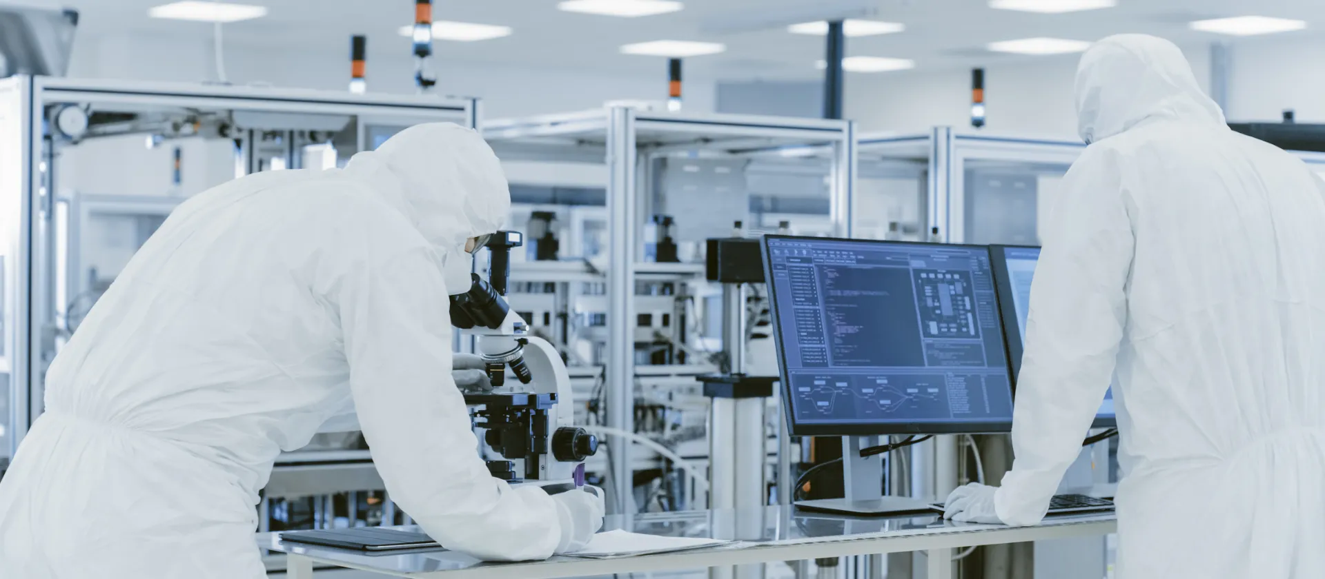 Personnel in cleanroom suits working with microscopes and digital systems in a laboratory, symbolizing manufacturing and laboratory excellence, digitalization, process harmonization, and MES/LIMS implementation.