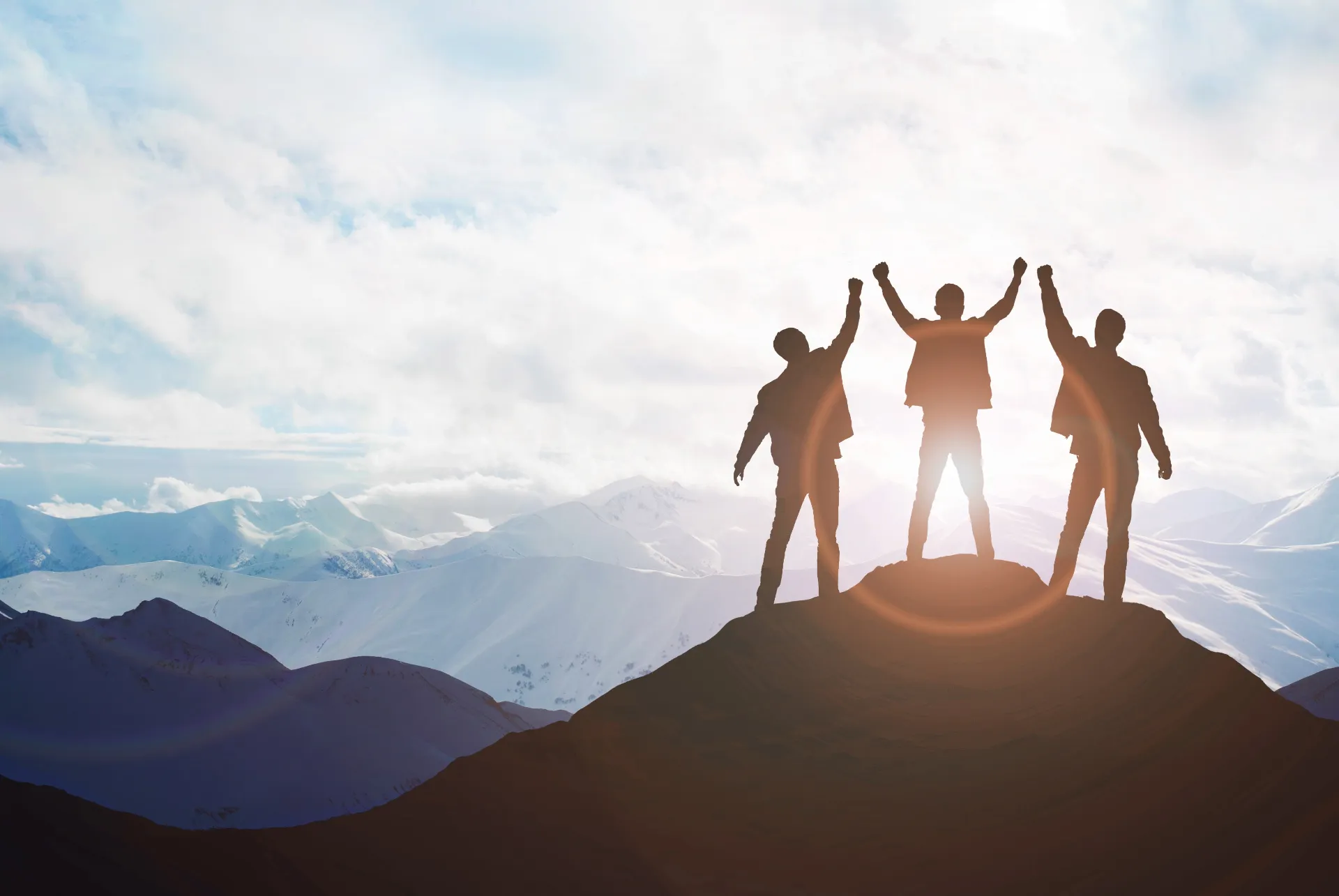 Symbolic image of corporate values Empowering – Three people on a mountain peak raise their arms in celebration.